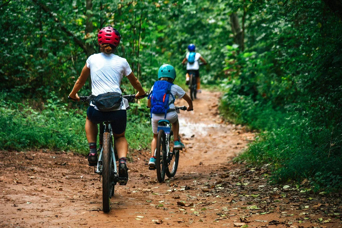A lively scene featuring bicyclists riding along a dirt path surrounded by lush greenery. The active setting suggests adventure and exploration, ideal for family outings and enjoying the outdoors together.
