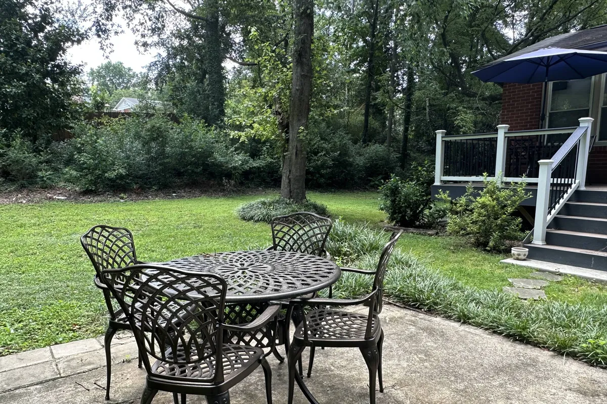 Showing the exterior with a metal table, chairs, lush green lawn, tree canopy, and the house facade in the background, this image highlights an inviting outdoor gathering space. It suggests opportunities for morning coffee, casual meetings, or unwinding after work, reinforcing the section’s emphasis on exploration and enjoyment beyond the home’s interior.