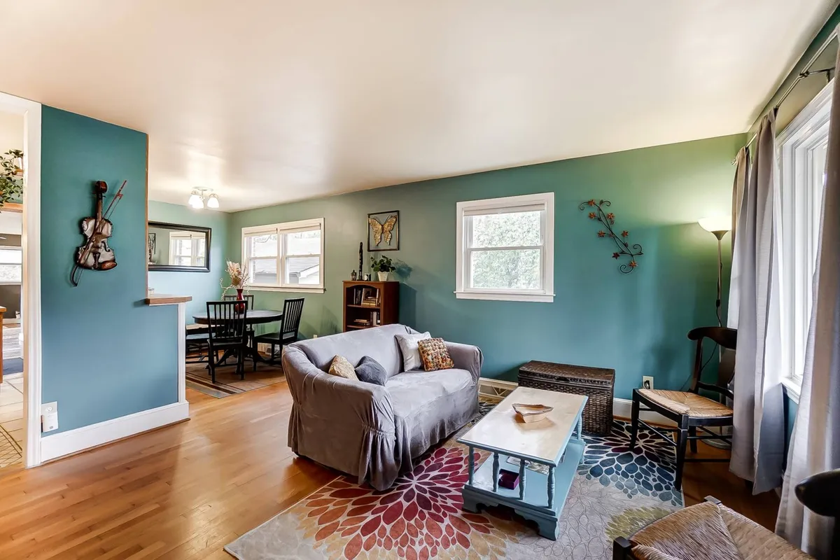This interior shot presents a comfortable sofa, a coffee table, and a dining area accented with decorative wall art. The open-plan layout fosters socialization and relaxation, with ample seating for groups to gather for dining or leisure activities. Sunlight streams in, enhancing the welcoming atmosphere.