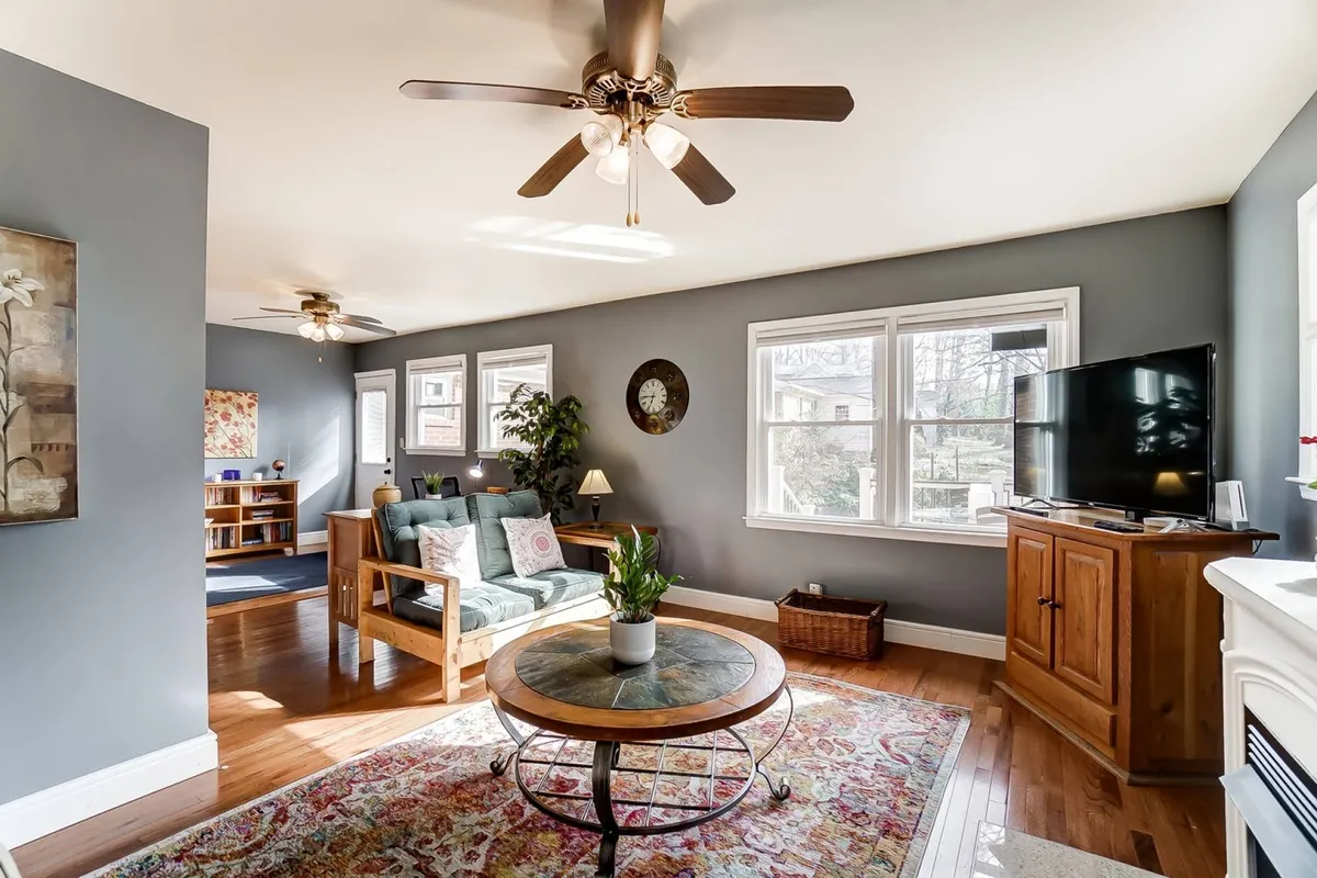 This image features a comfortable sofa, a coffee table, and a TV against a backdrop of large windows. The arrangement is ideal for watching movies, streaming shows, or lively game nights, all under natural light that adds to the inviting feel.