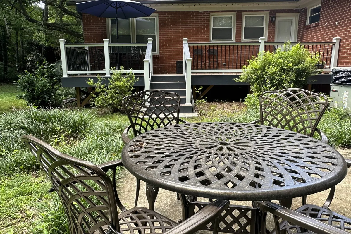 This image features an inviting outdoor dining area with a metal table, chairs, umbrellas, lush greenery, and the brick exterior of the house, setting the stage for relaxed social gatherings and al fresco meals.
