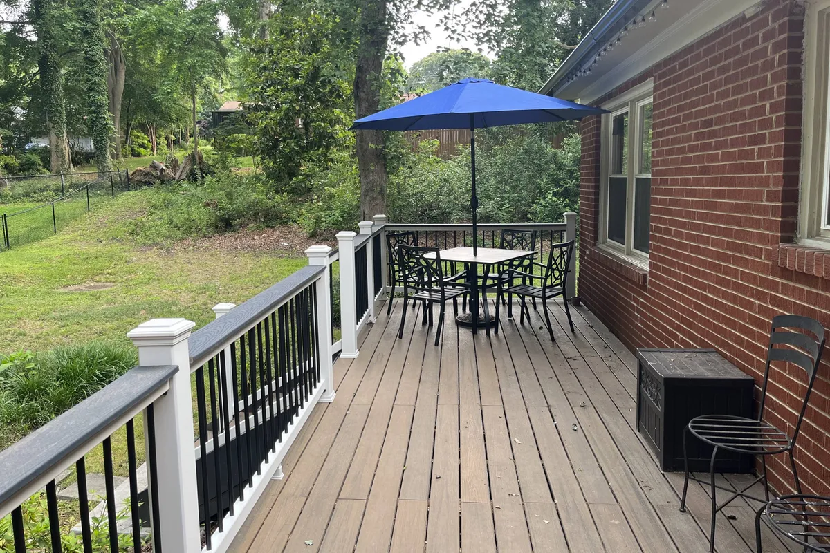 An inviting exterior patio area featuring a table and chairs under a blue umbrella, all set against a charming brick wall. The scene suggests a tranquil outdoor space ideal for dining, relaxing, or enjoying social time with pets in the fresh air.